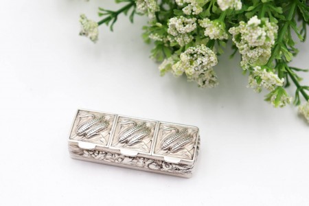 Caixa de comprimidos em prata com três divisórias e maçarocas de milho em relevo